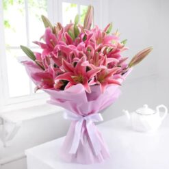A bouquet of pink lilies wrapped in tissue paper, a delicate and elegant floral arrangement perfect for any occasion.