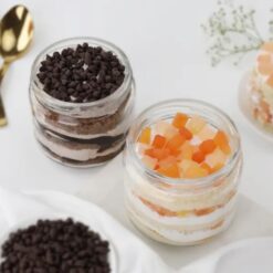 Glass jars filled with layers of mixed fruit and chocochip cakes, a delicious combination for dessert lovers.