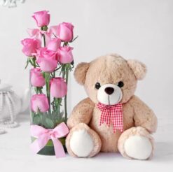 A vase filled with ten pink roses accompanied by a teddy bear, a charming gift for expressing affection and sweetness.