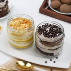 Glass jars filled with layers of butterscotch and chocochip cakes, a delectable combination for dessert enthusiasts.